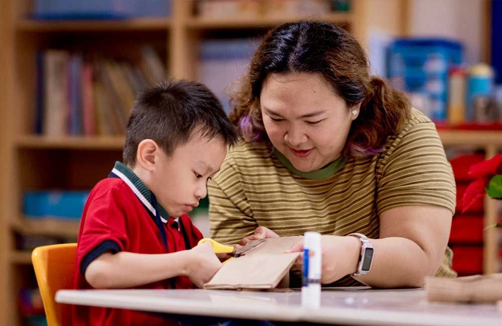A woman is helping a young boy with his homework at a table.