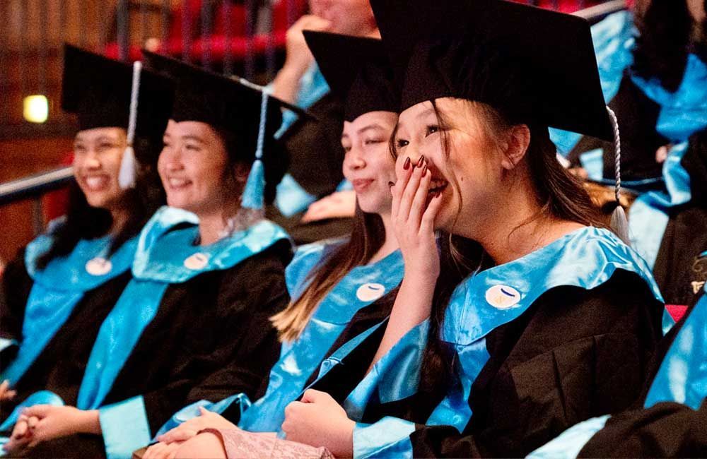 A group of graduates are sitting in a row and laughing.