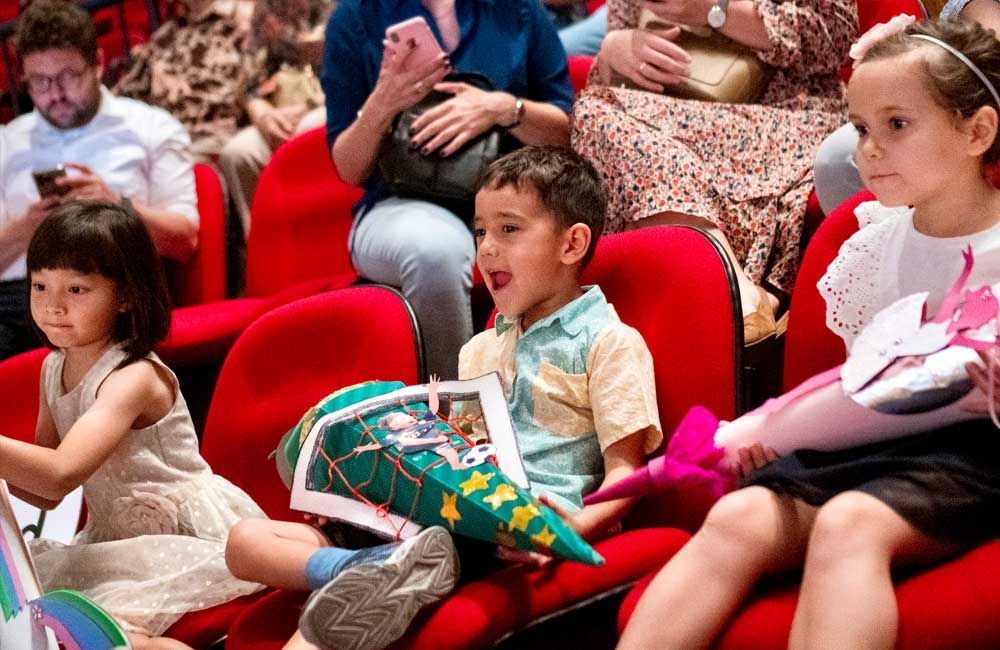 A group of children are sitting in red chairs in a theater.
