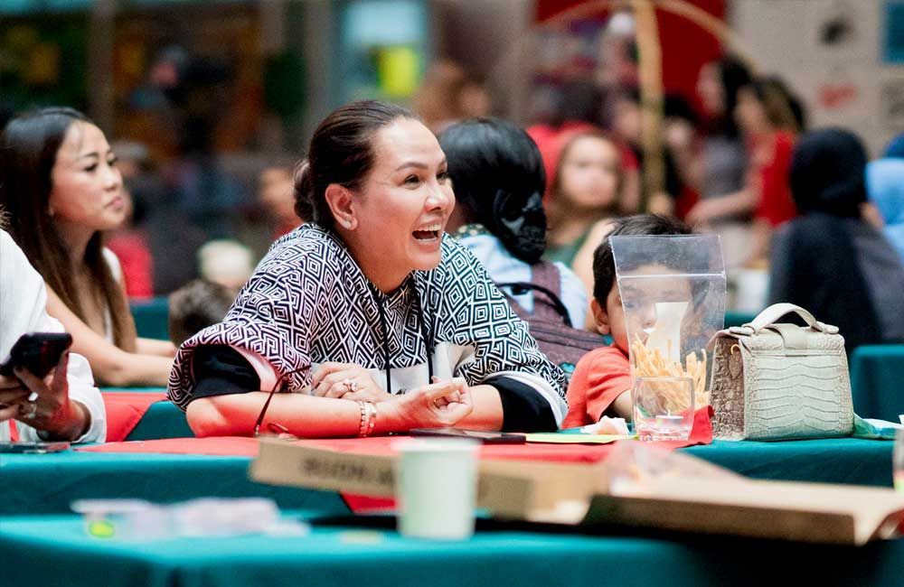 A woman is sitting at a table in front of a crowd of people.