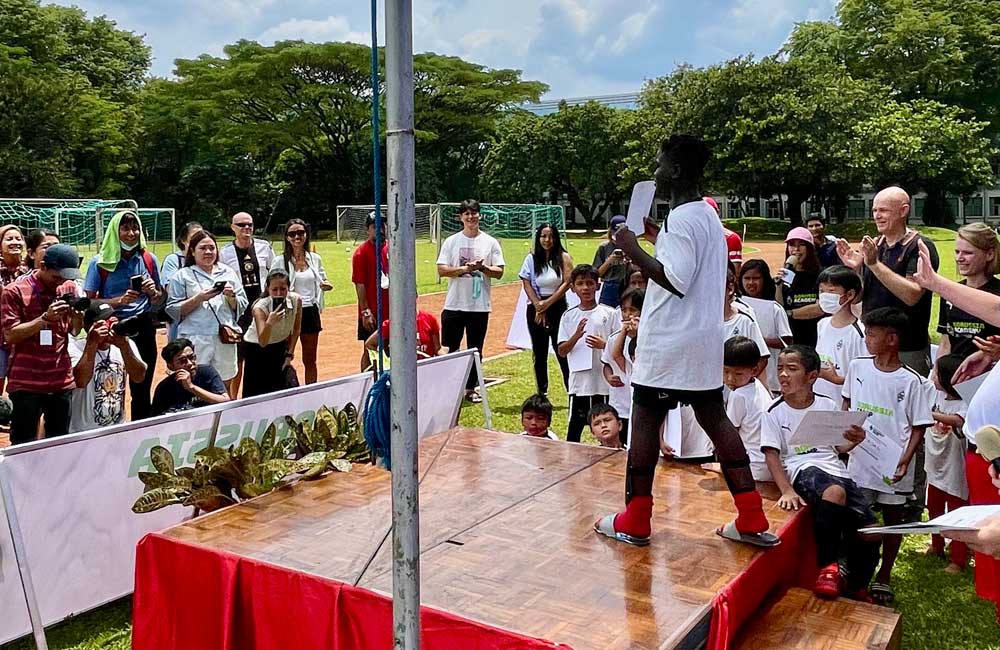 A woman is standing on a stage in front of a crowd of children.