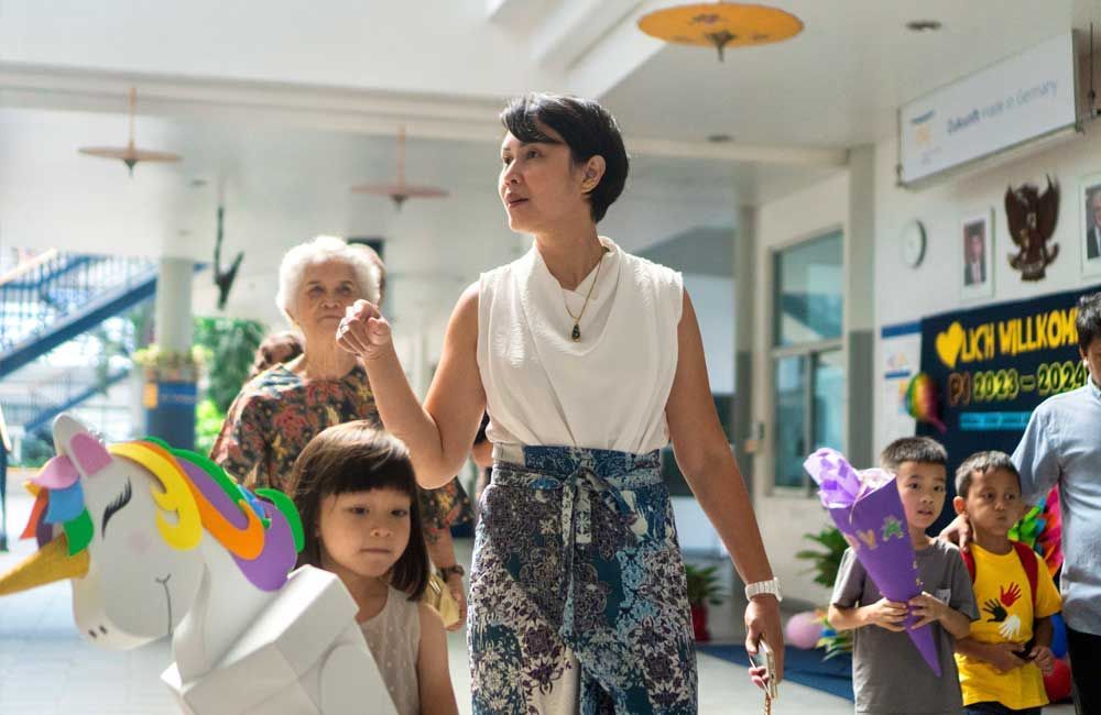 A woman is walking down a hallway with a group of children.