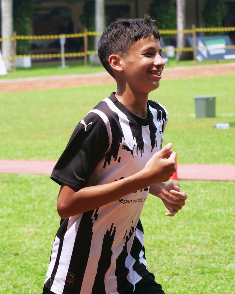 A young boy in a black and white striped shirt is running on a field