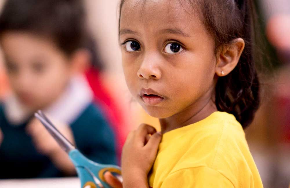 A young girl in a yellow shirt is holding a pair of scissors.