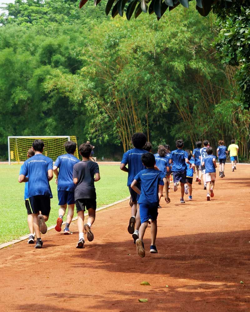 A group of children in blue shirts are running on a dirt track