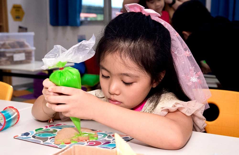 A little girl is decorating cookies with a green bag.