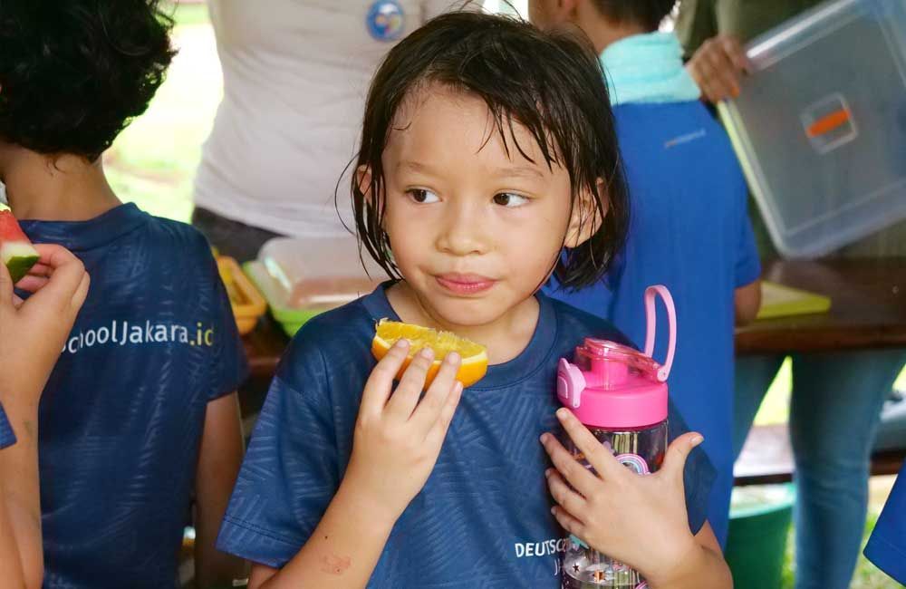 A little girl is eating an orange and holding a water bottle.