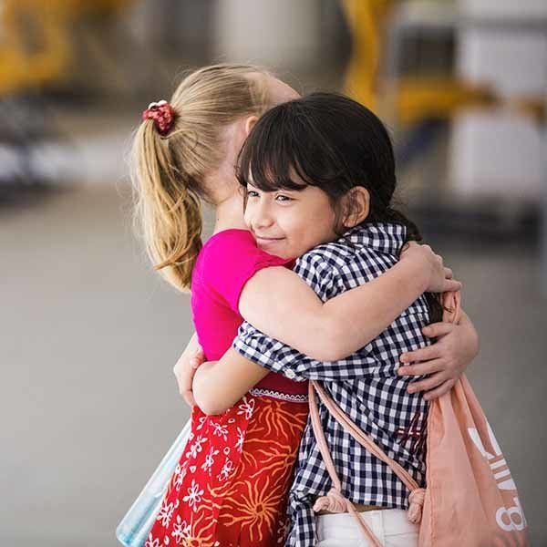 Two little girls are hugging each other and one of them is wearing a bag that says ' t & t ' on it