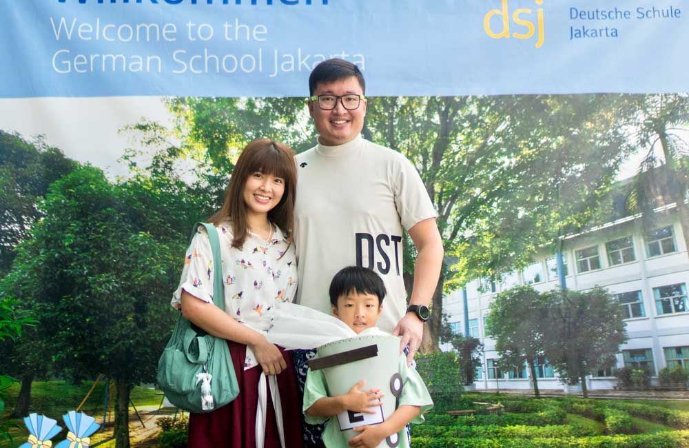 A family is posing for a picture in front of a sign that says welcome to the german school jakarta.