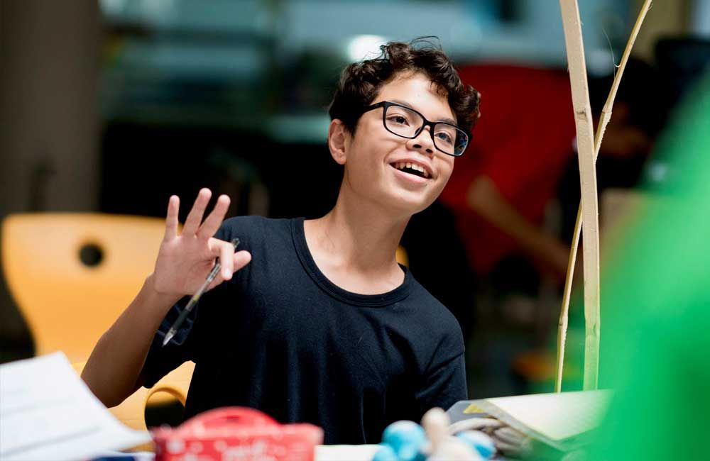 A young boy wearing glasses is sitting at a table with a pen in his hand.