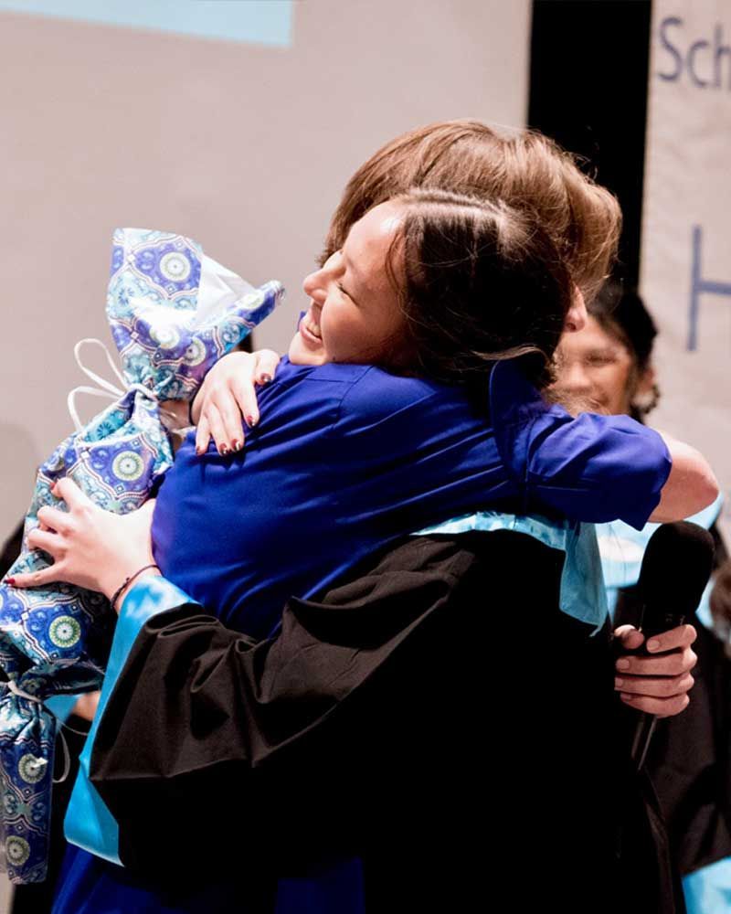 A woman in a graduation cap and gown is hugging another woman