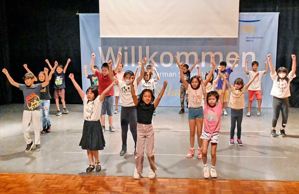 A group of children are standing on a stage with their arms in the air.