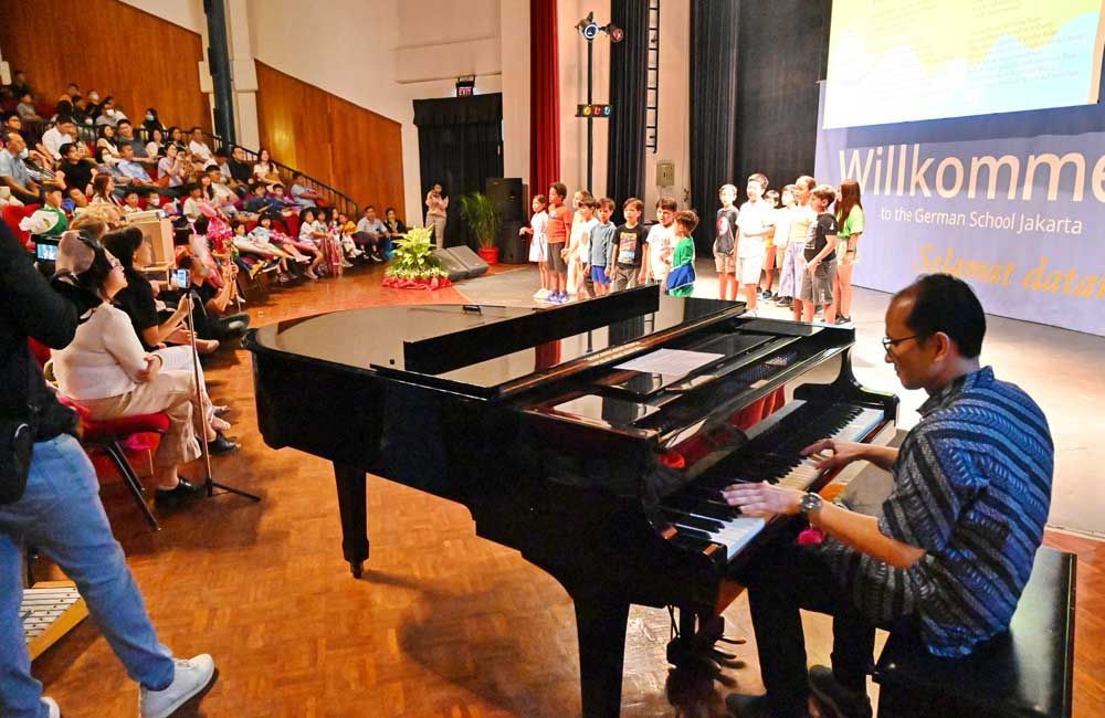 A man is playing a piano in front of a crowd and a sign that says willkommen