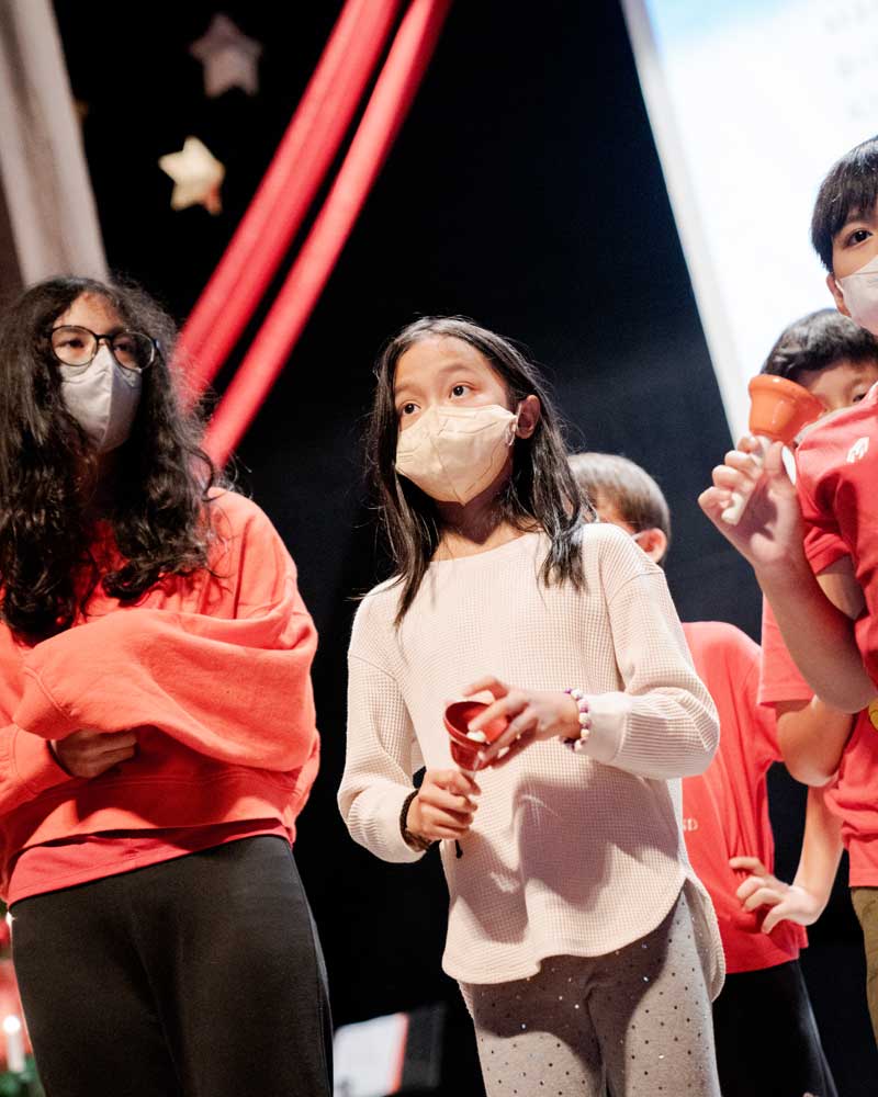 A group of children wearing face masks are standing on a stage.