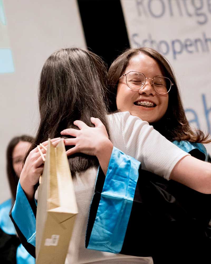 A woman in a graduation cap and gown is hugging another woman