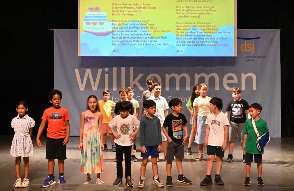 A group of children are standing on a stage in front of a large screen.
