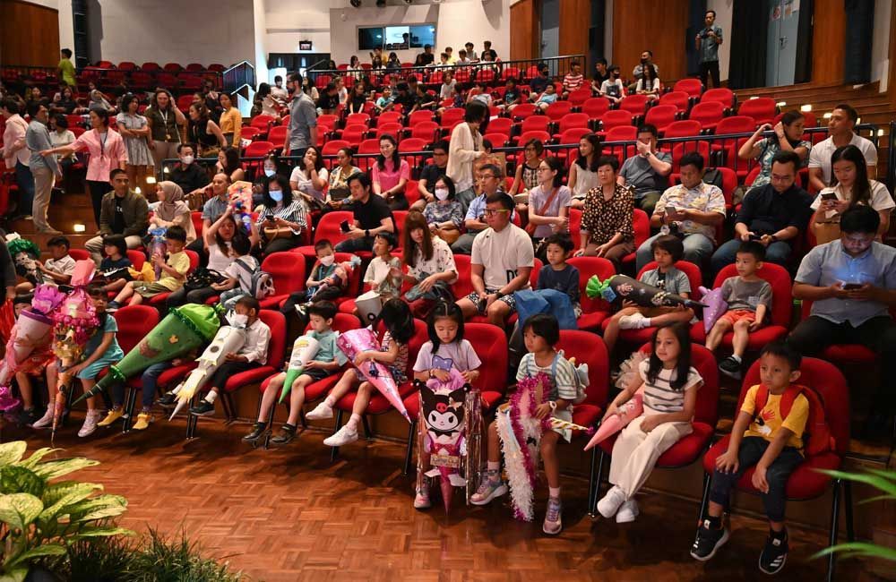 A large group of people are sitting in red chairs in an auditorium.