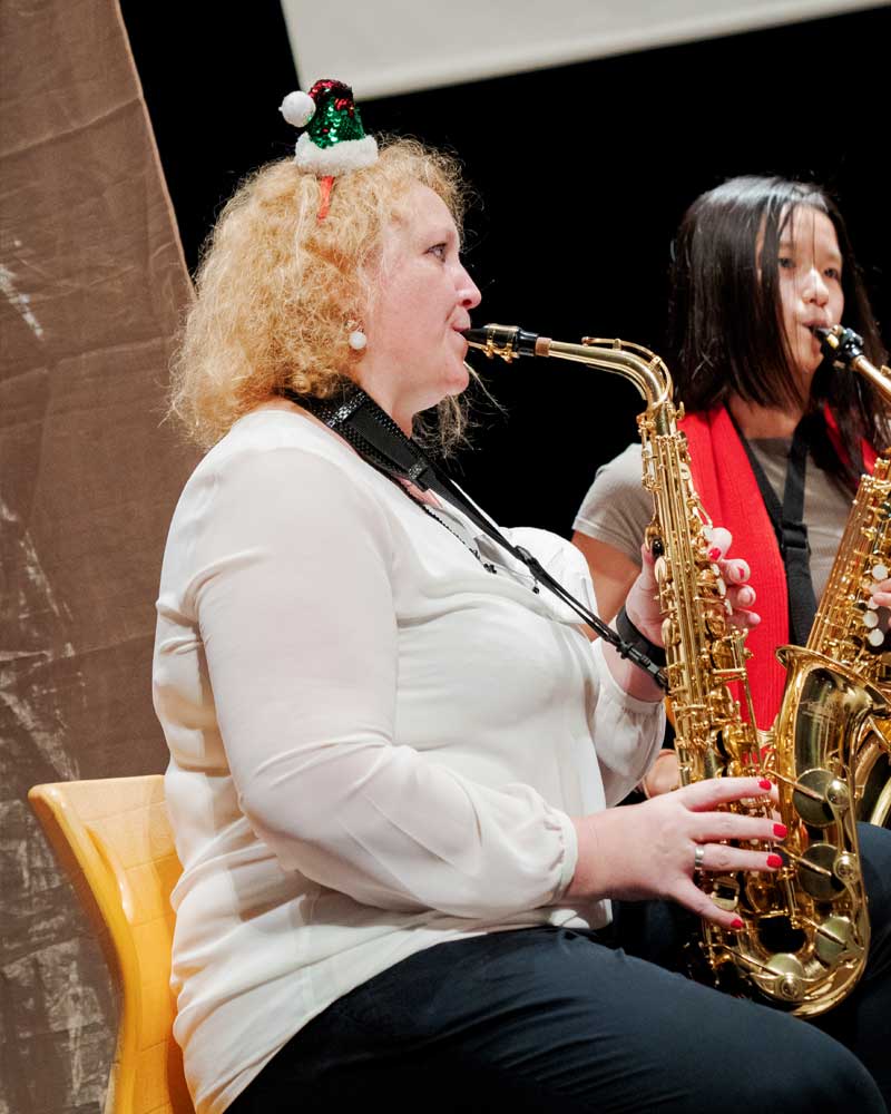 A woman wearing a santa hat is playing a saxophone