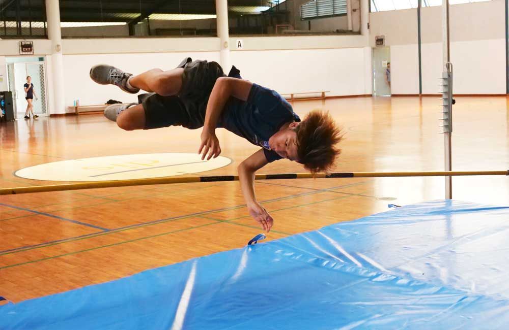 A person is jumping over a pole in a gym.