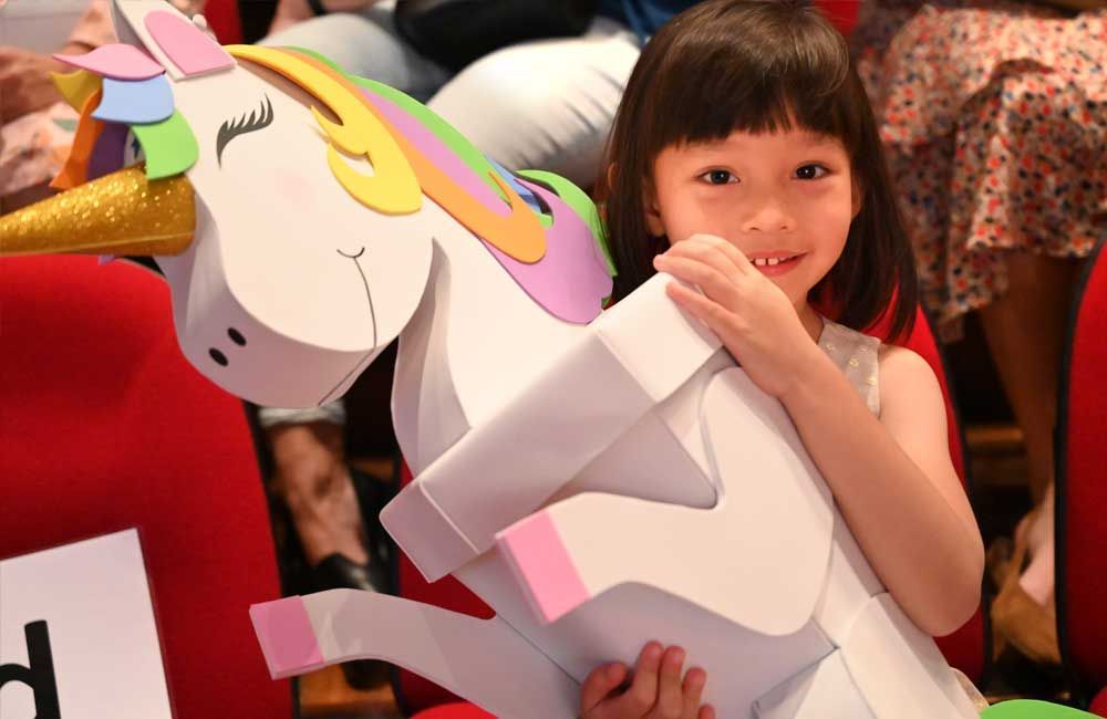 A little girl is holding a paper unicorn in her hands.