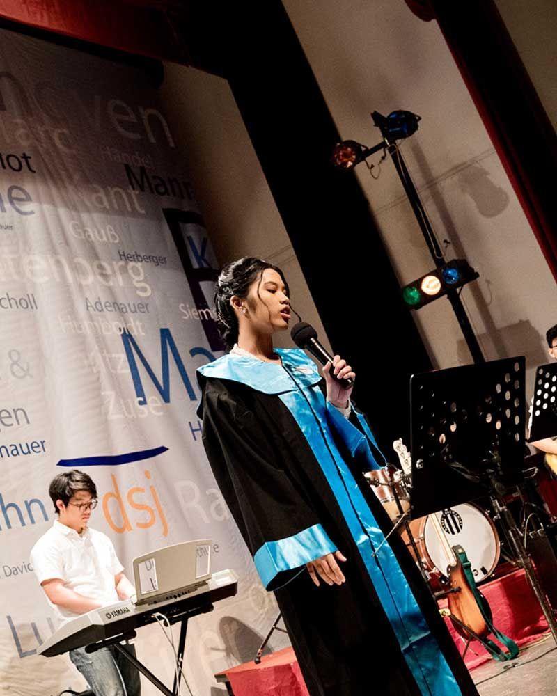 A woman in a graduation gown singing into a microphone