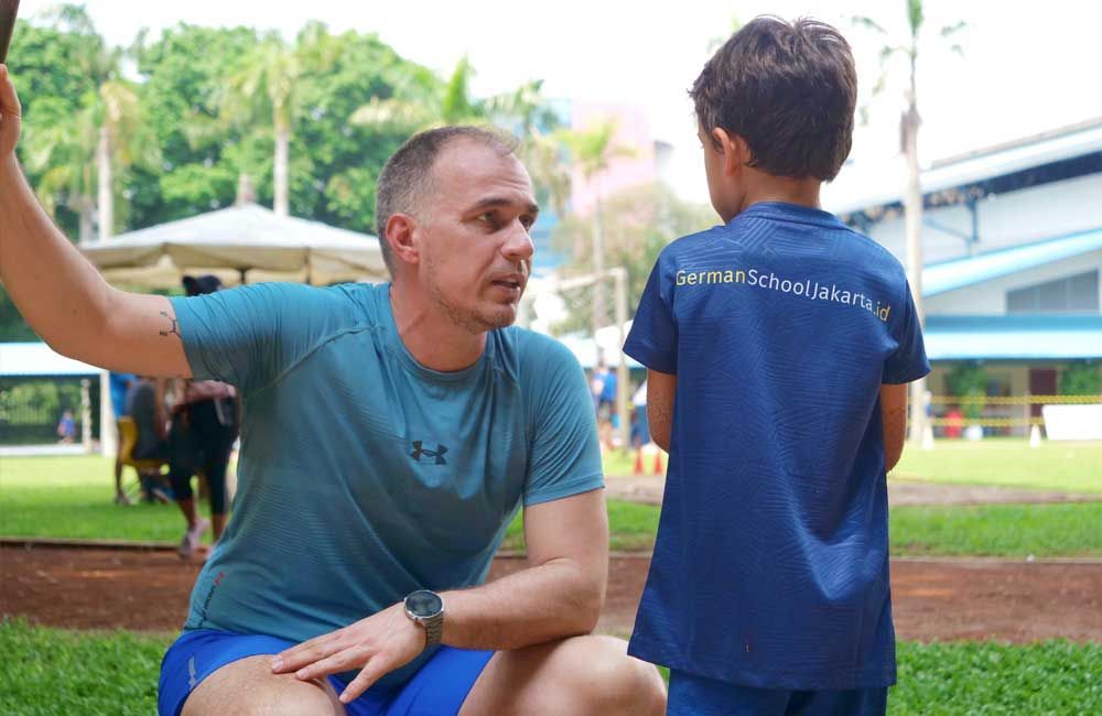 A man is kneeling down next to a little boy in a blue shirt.