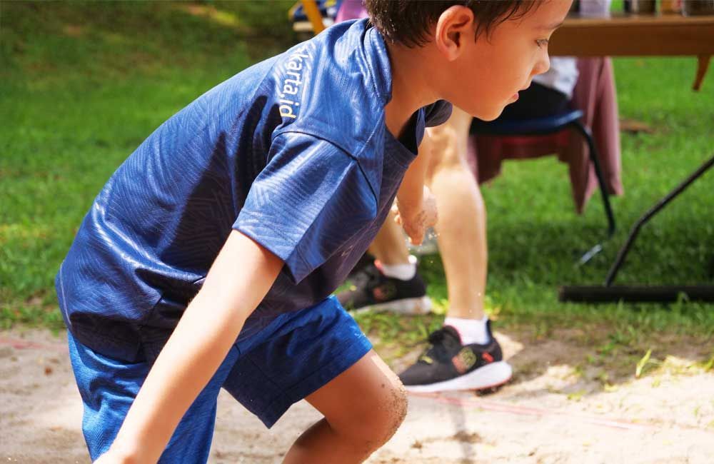 A young boy in a blue shirt and blue shorts is running in the dirt.