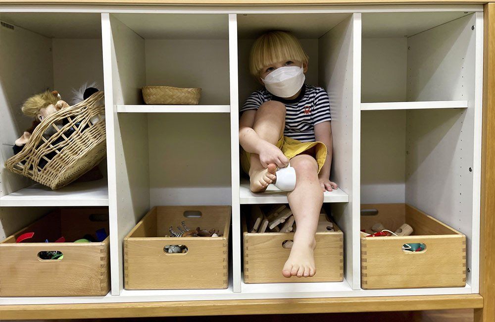 A little boy wearing a mask is sitting on a shelf.