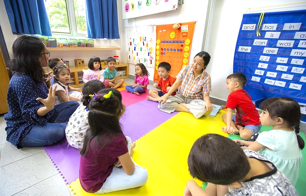 A group of children are sitting on the floor in a circle with a teacher.