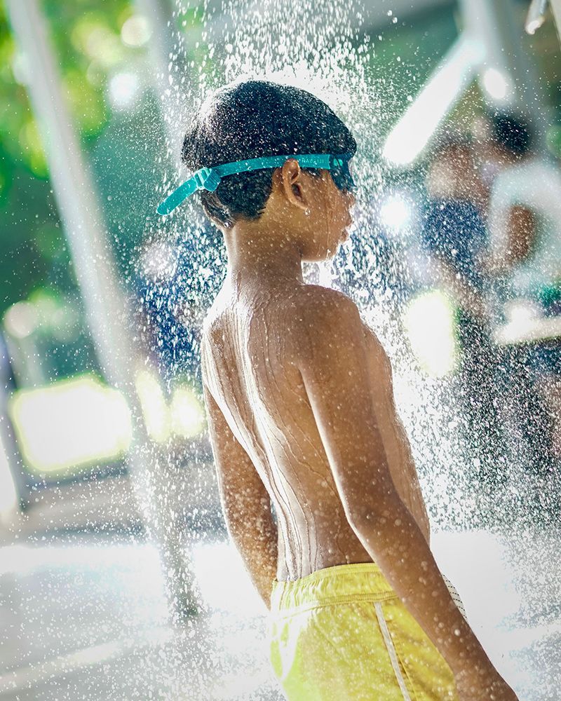 A young boy wearing goggles is standing in a spray of water.