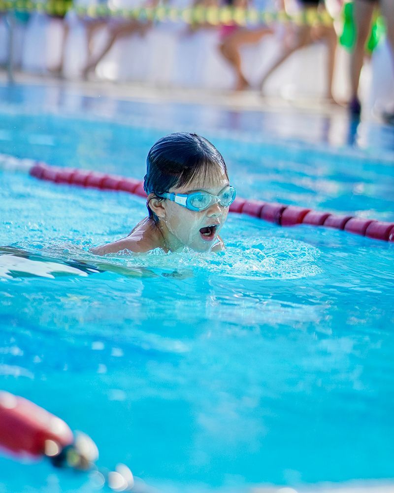 A young girl wearing goggles is swimming in a swimming pool.