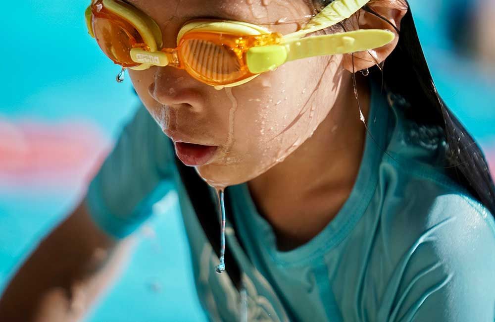 A young girl wearing goggles is swimming in a pool.