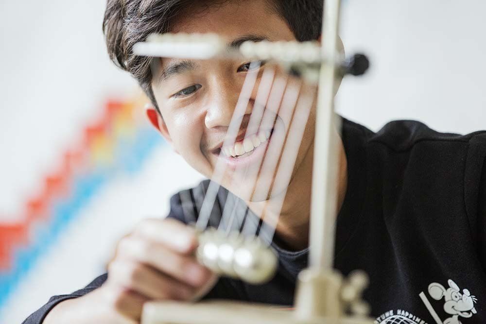 A young man is playing with a pendulum and smiling.