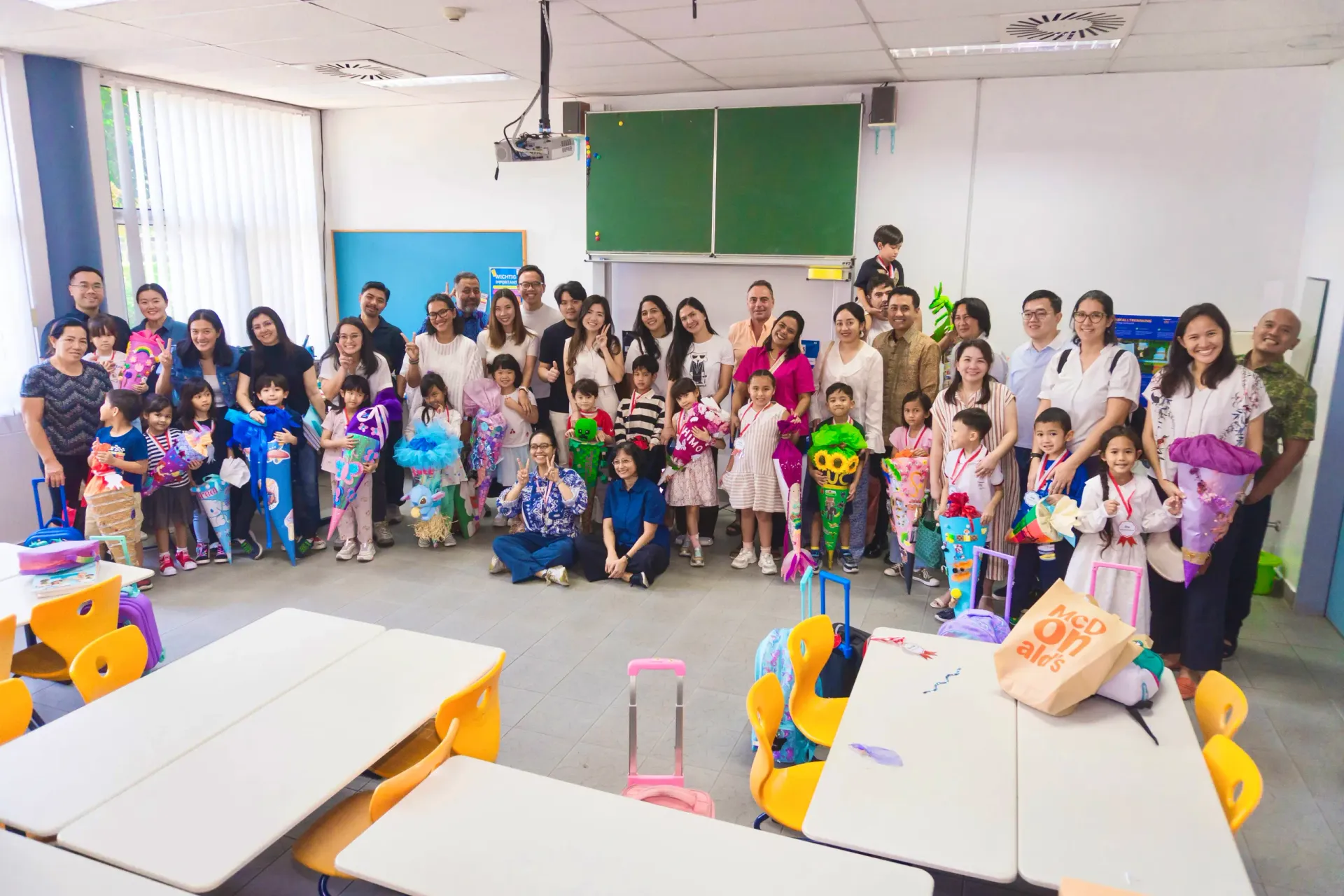 Group photo of children and adults in a classroom setting.