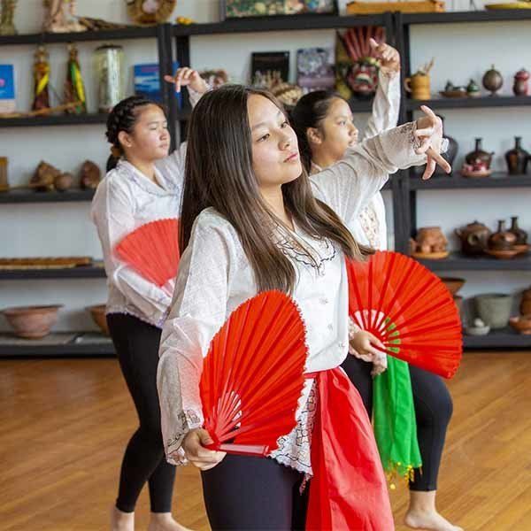 Three women are dancing with red fans in a room.