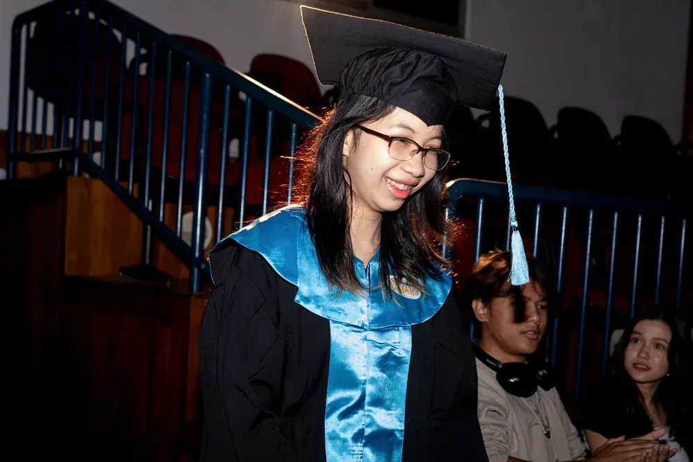 A woman is wearing a graduation cap and gown and smiling.