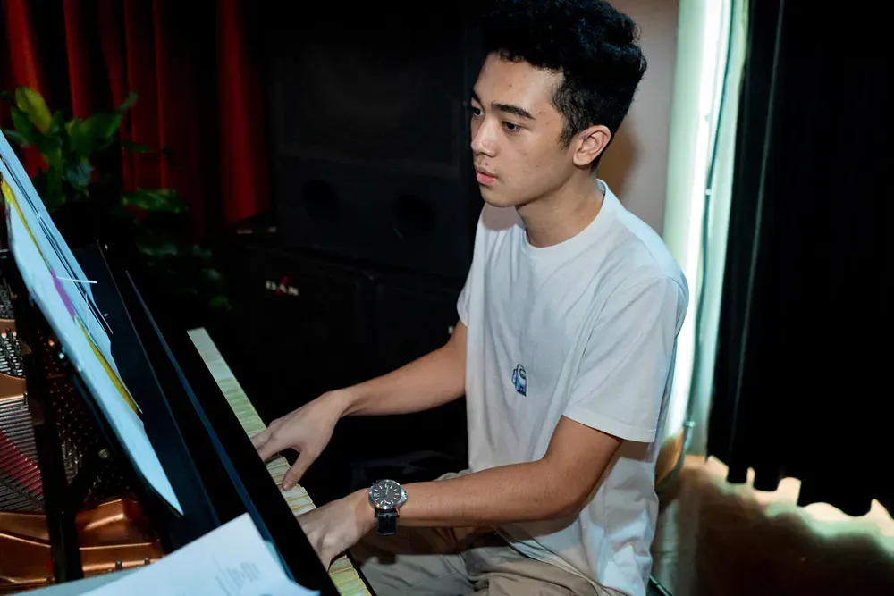 A young man in a white shirt is playing a piano.