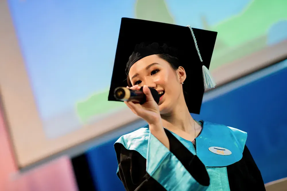 A woman in a graduation cap and gown is singing into a microphone.