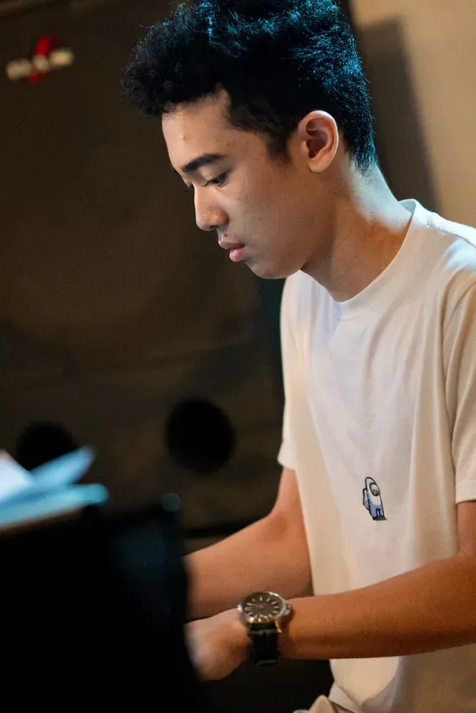 A young man wearing a white t-shirt and a watch is playing a piano.