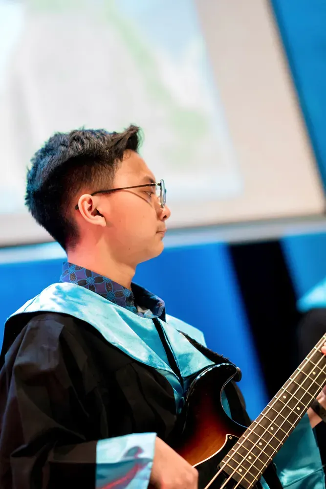 A man in a graduation gown is playing a guitar