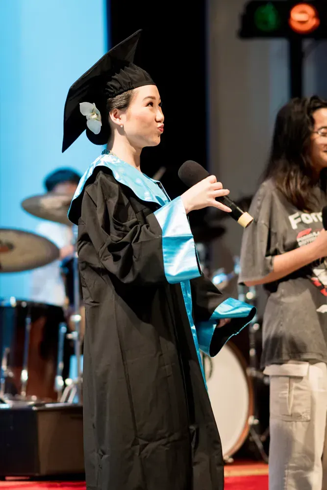 A woman in a graduation cap and gown is speaking into a microphone.
