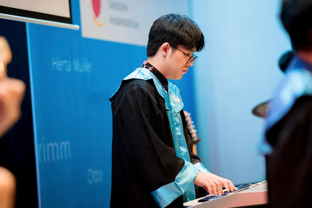 A man in a graduation gown is playing a keyboard.