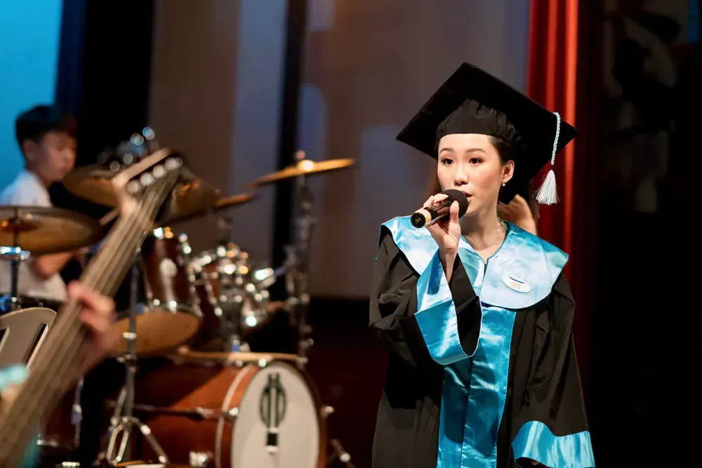 A woman in a graduation cap and gown is singing into a microphone