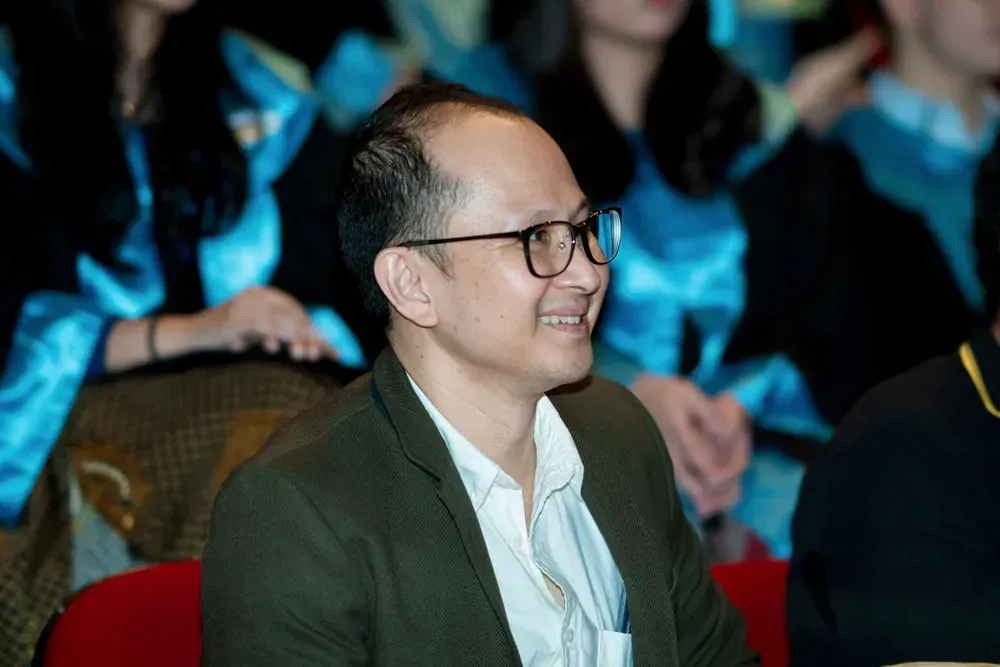 A man wearing glasses is sitting in a crowd of people.