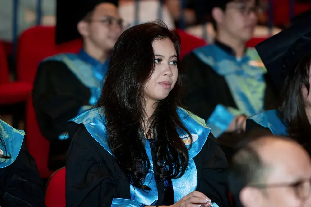 A woman in a graduation cap and gown is sitting in a crowd of people.