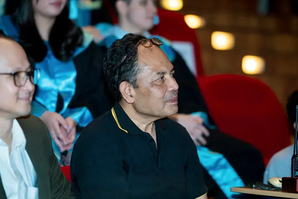 A man in a black shirt is sitting in a crowd of people at a graduation ceremony.