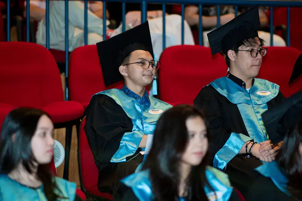 A group of graduates are sitting in red chairs at a graduation ceremony.