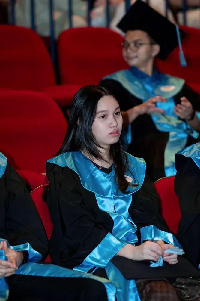 A woman in a graduation cap and gown is sitting in an auditorium.