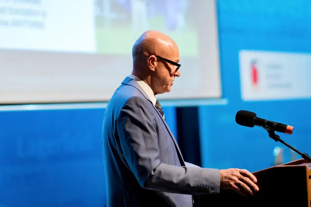 A man in a suit and tie is standing at a podium speaking into a microphone.