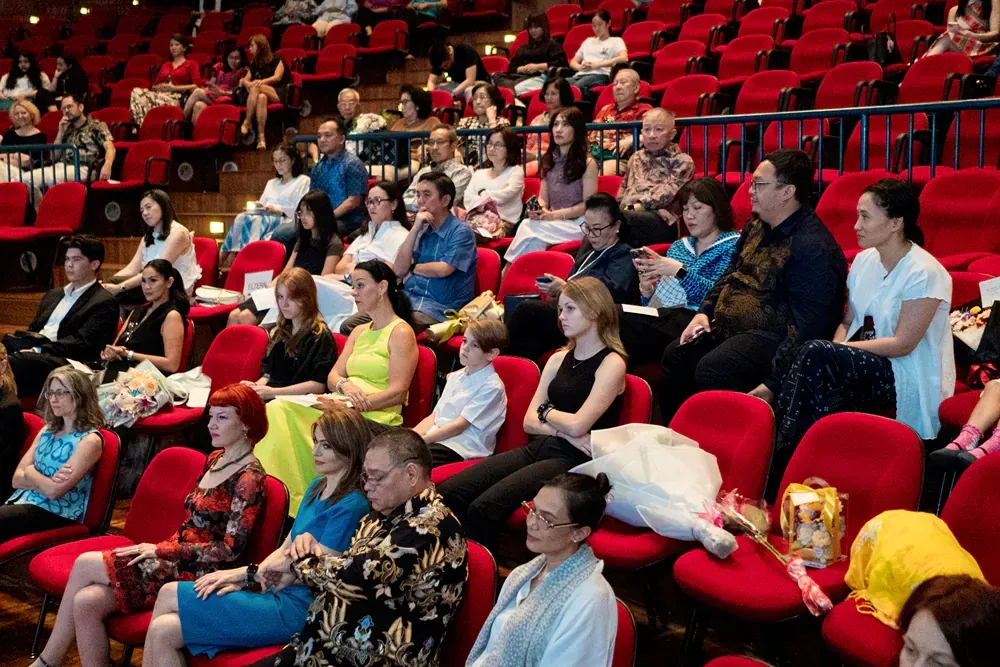 A large group of people are sitting in red chairs in an auditorium.